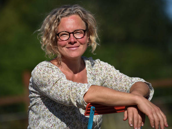 Hier ist Sandra zu sehen eine Frau mit mittellangen blonden lockigen Haaren und Brille wie sie in de Kamera lächelt